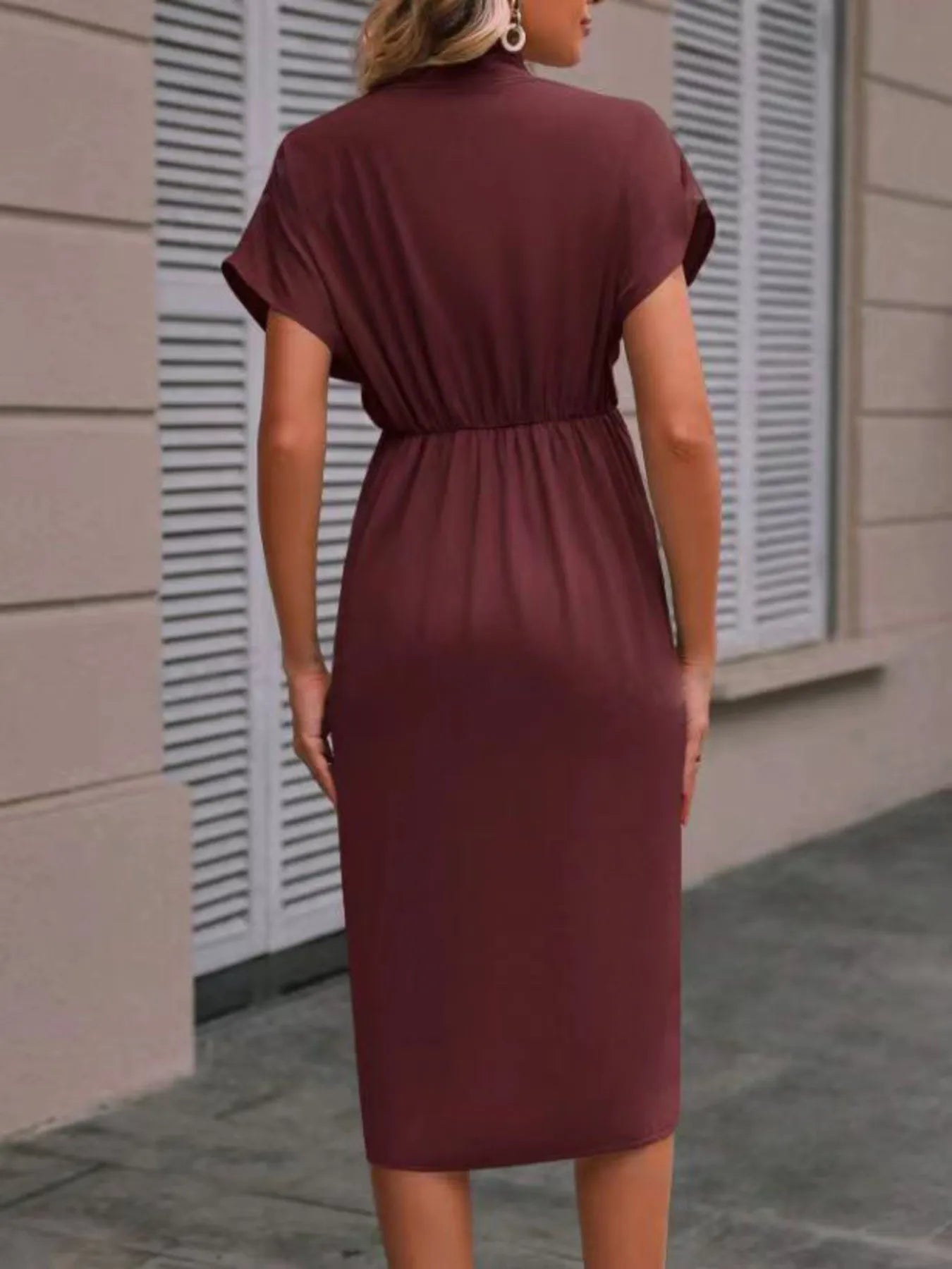 Woman wearing a burgundy dress standing against a beige wall.