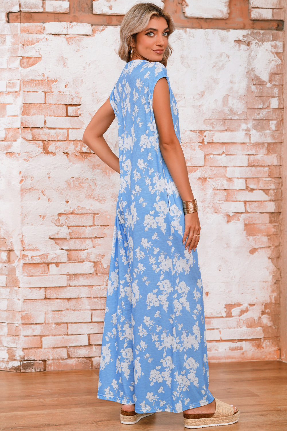 Woman wearing a blue floral dress against a brick wall.