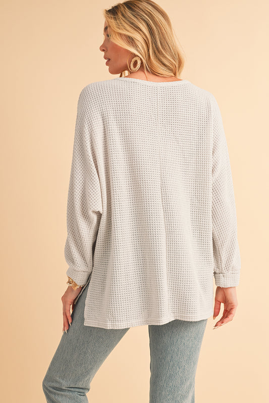 Woman wearing a textured beige top and light blue jeans on a beige background