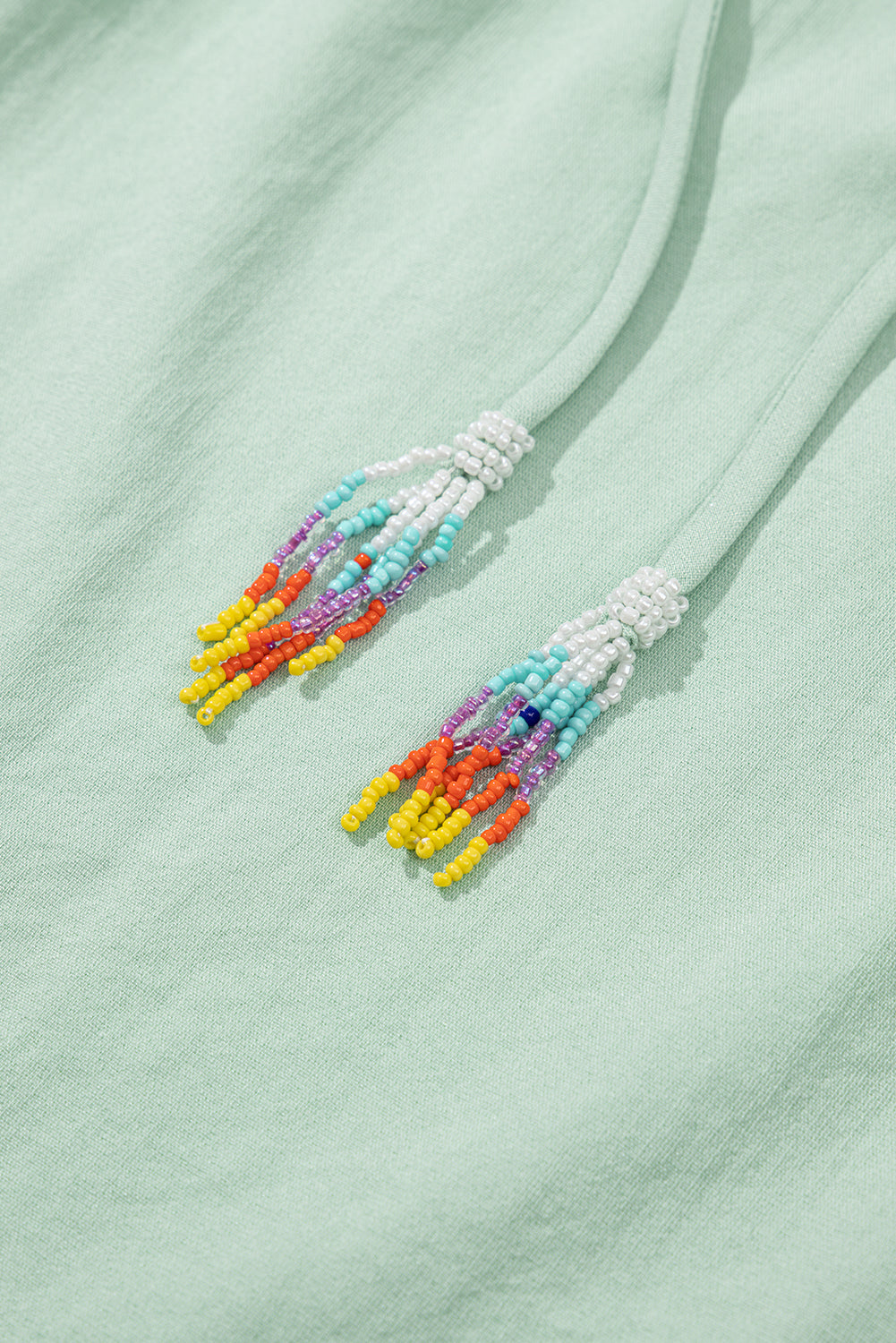 Close-up of colorful beaded earrings on a light green fabric background