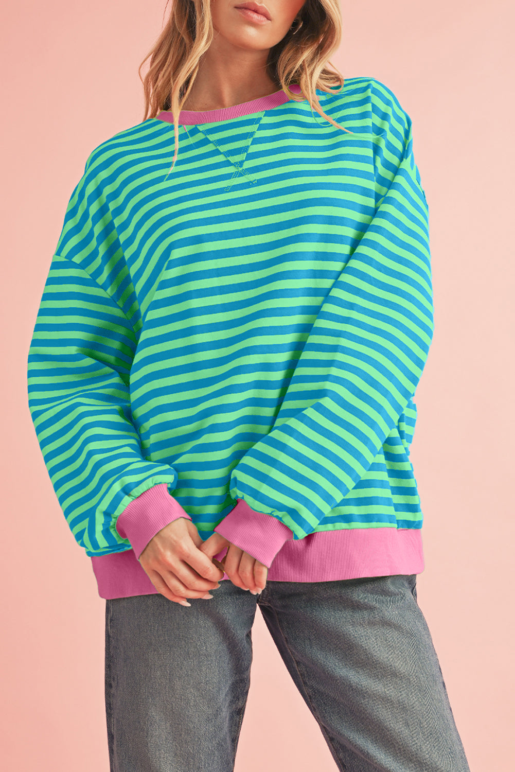 Person wearing a green and blue striped sweater with pink trim on a pink background