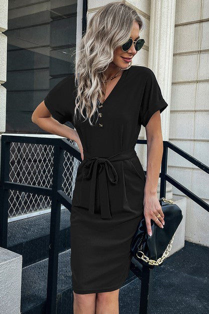Woman wearing a black dress with a belt, standing outdoors.