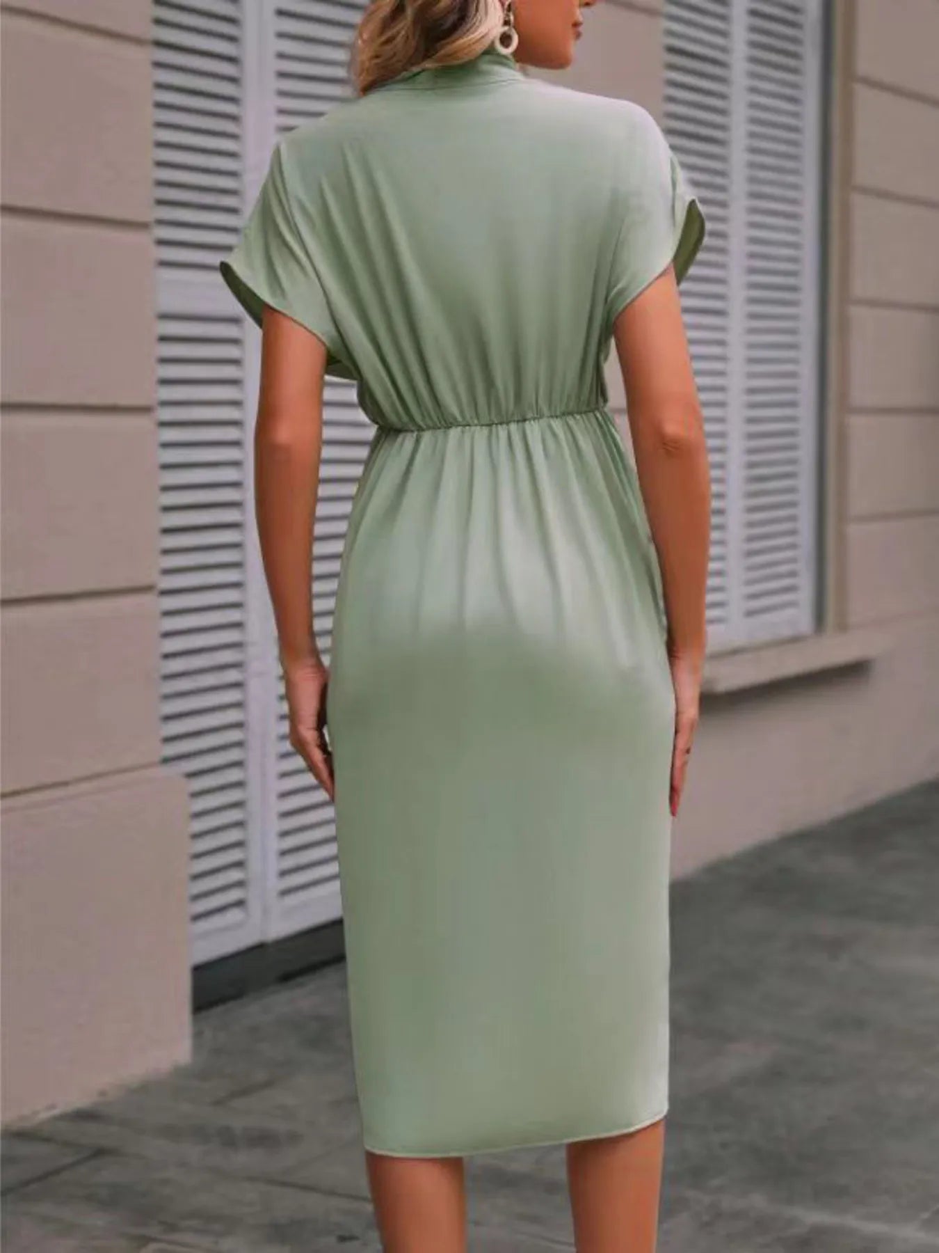 Woman wearing a green dress standing against a neutral wall.