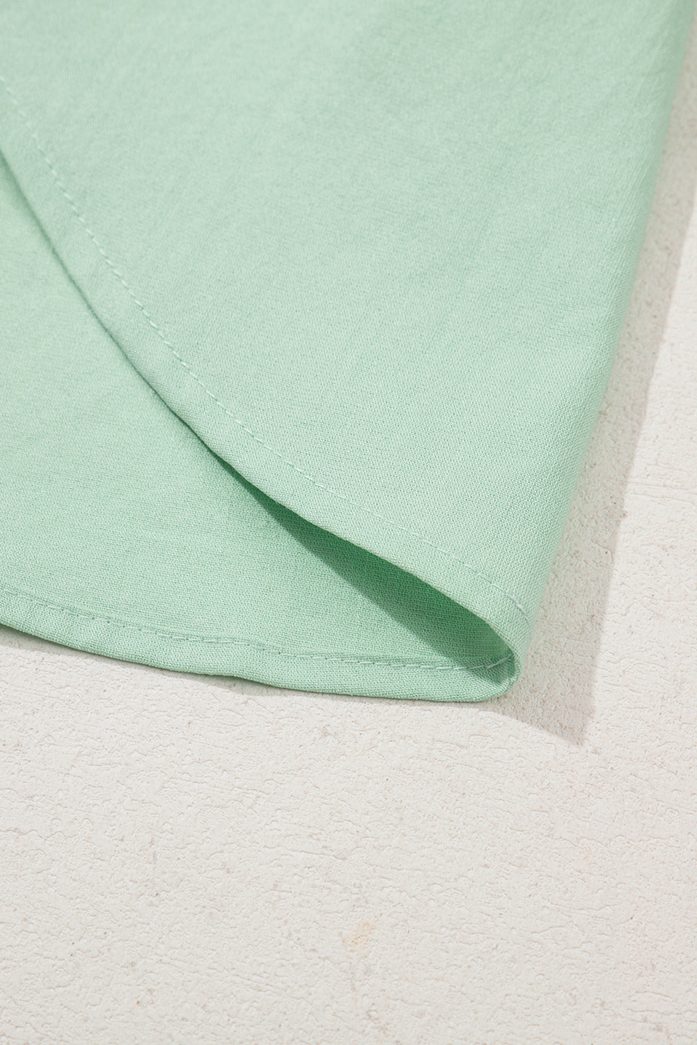 Close-up of a light green fabric corner on a textured beige surface
