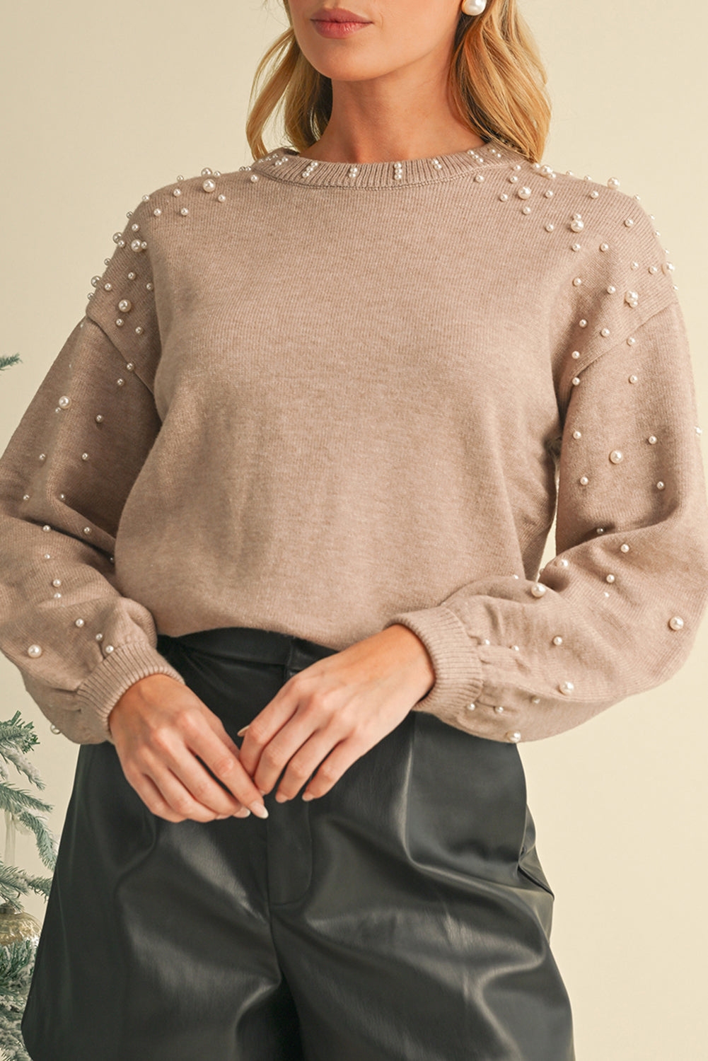 Beige sweater with pearl embellishments worn by a person against a neutral background