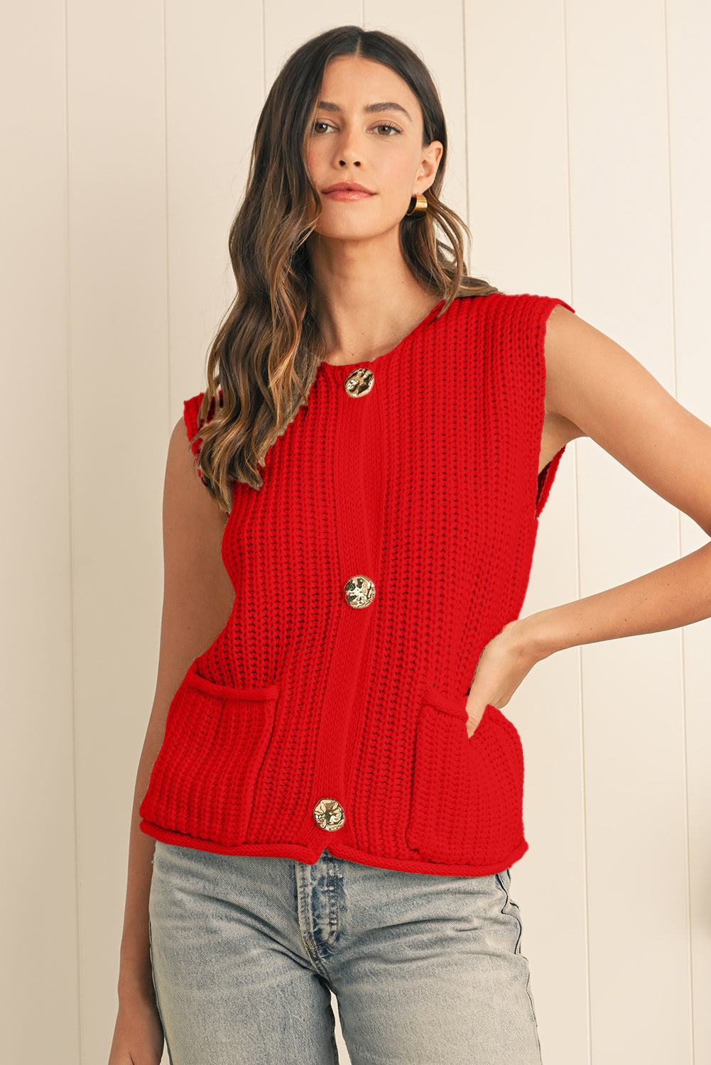 Woman wearing a red sleeveless knitted top with buttons against a light wooden panel background