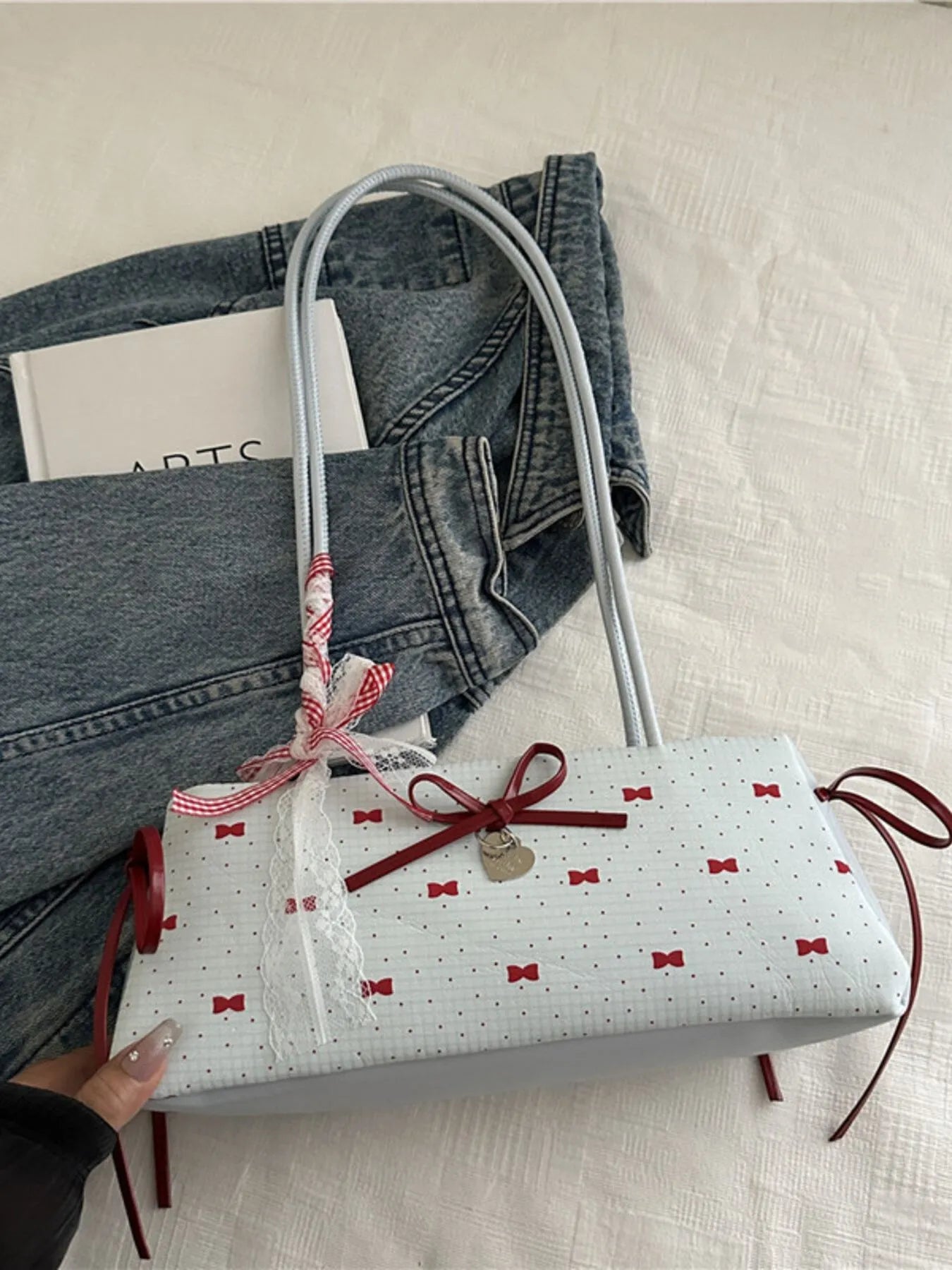 White handbag with red bow design held by a hand on a light background