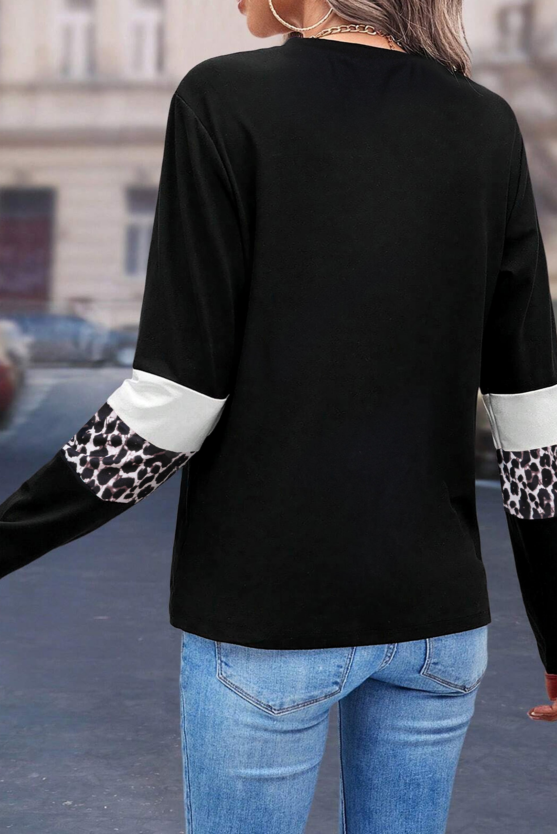 Black long-sleeve top with leopard print cuffs and hem worn by a person on a street.