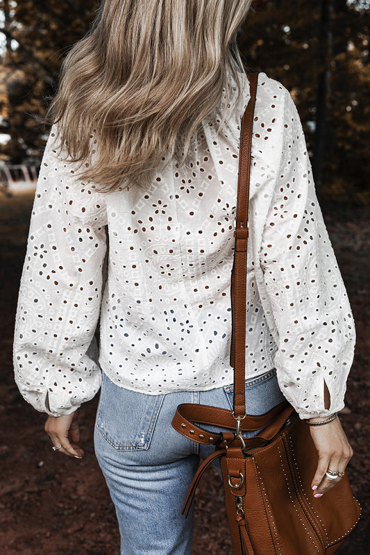 Person wearing a white blouse with black polka dots and blue jeans, holding a brown leather bag.