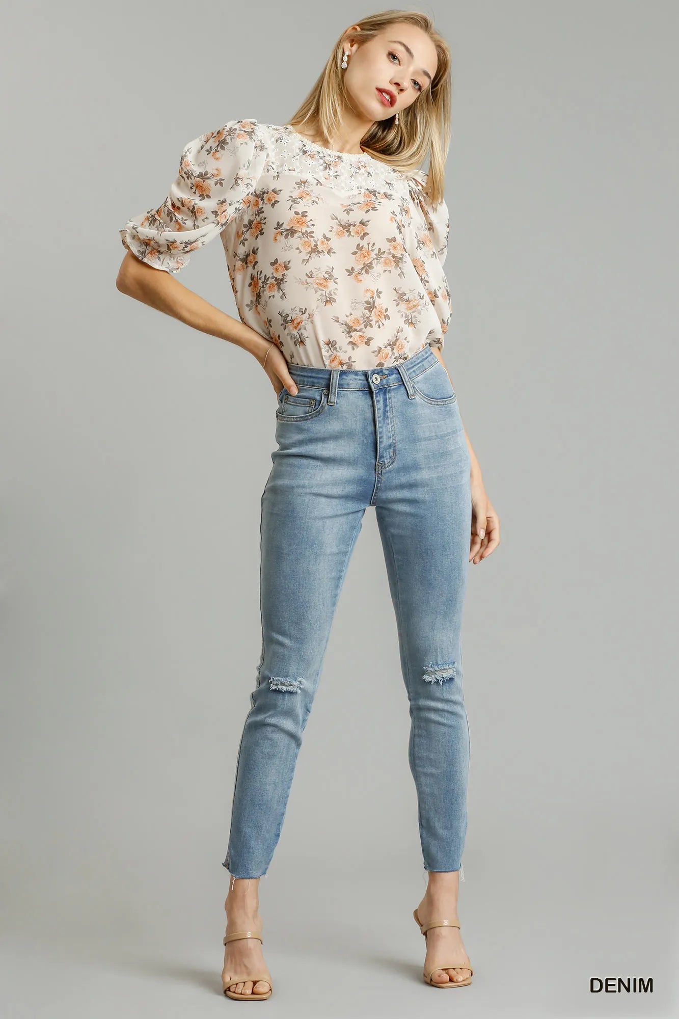 Woman wearing a floral blouse and blue jeans on a gray background