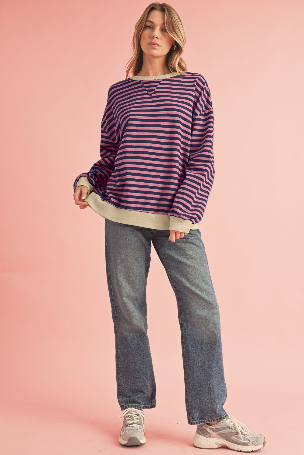 Woman wearing a striped sweater and jeans on a pink background