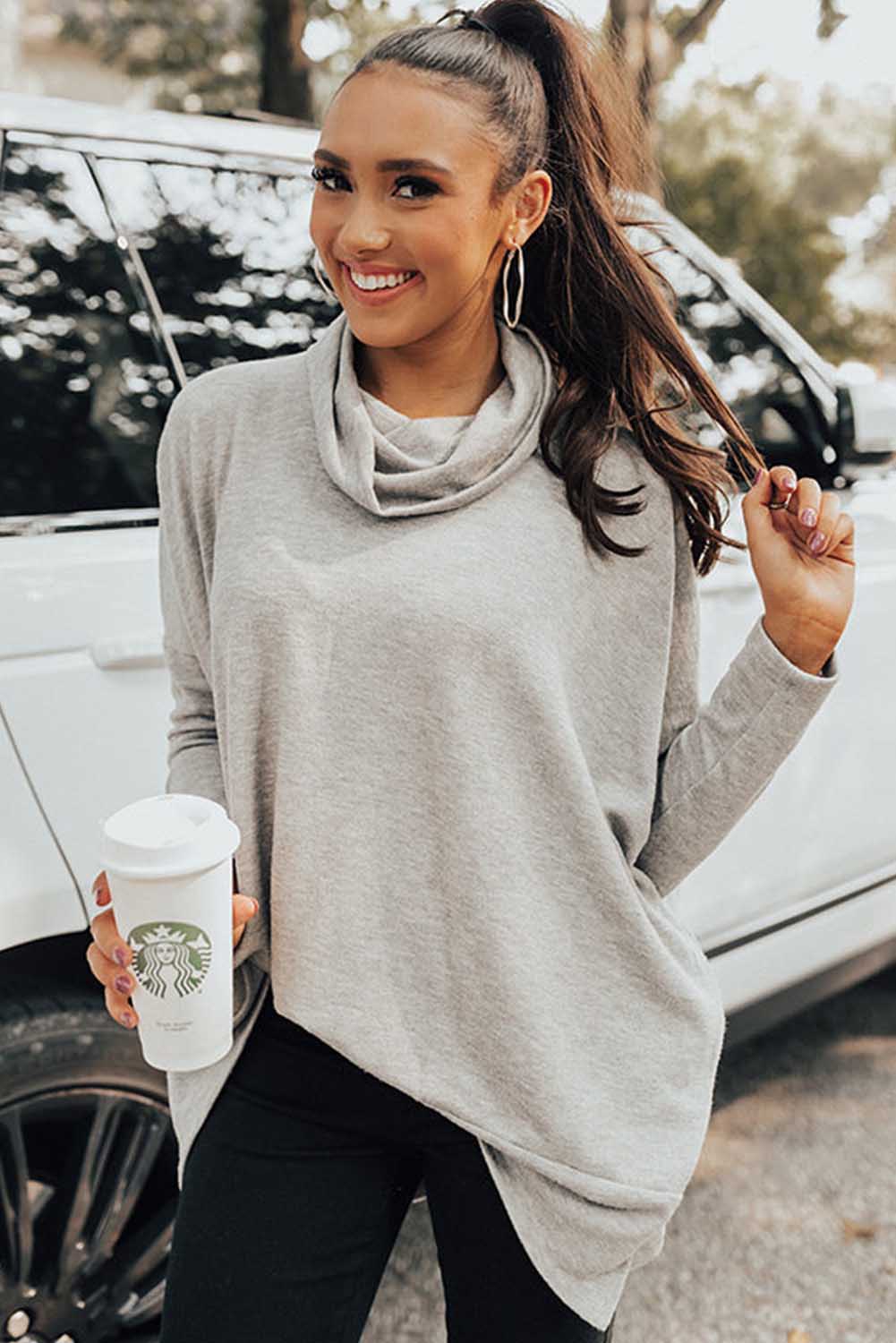 Woman in a gray sweater holding a Starbucks cup outdoors.