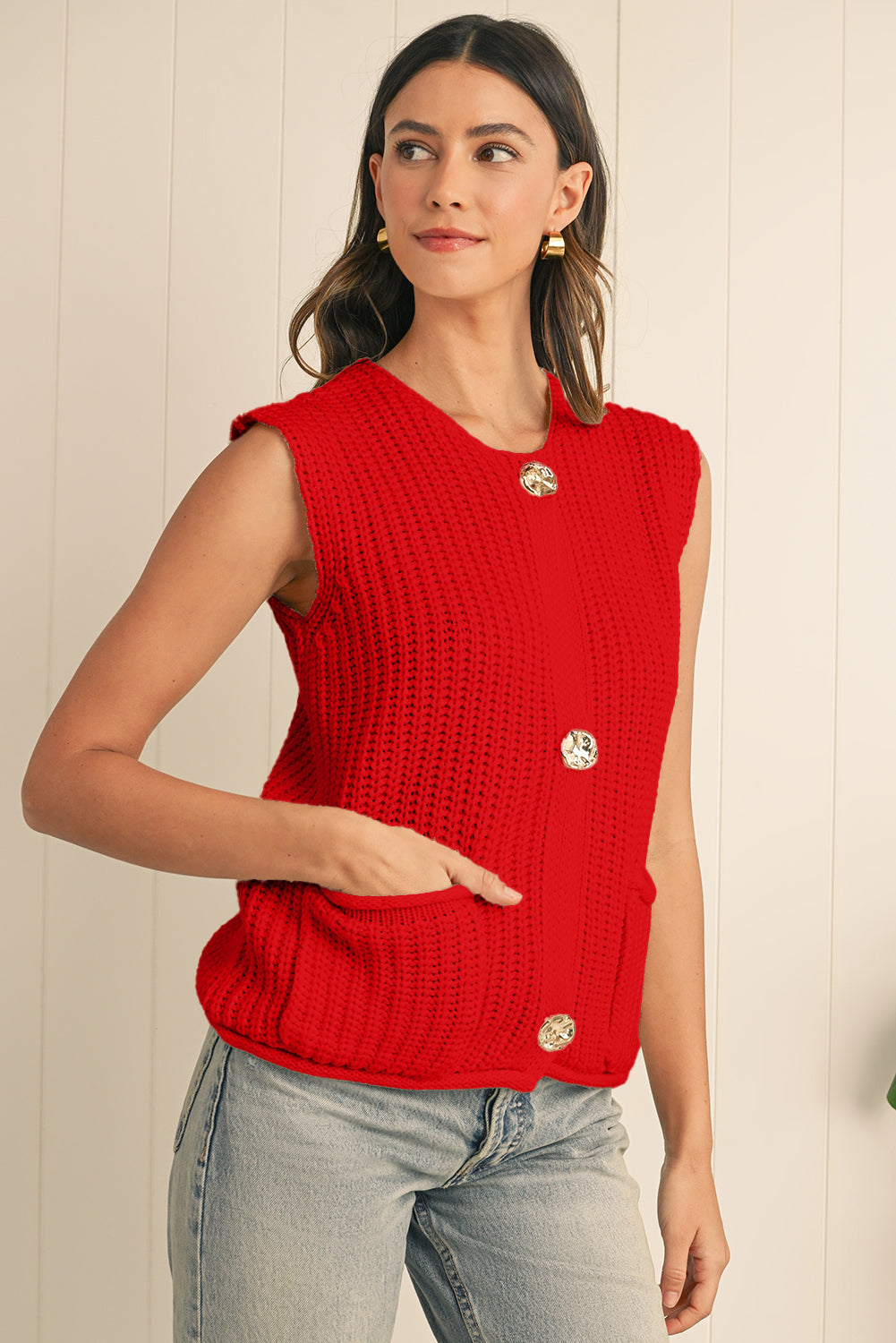 Woman wearing a red knitted vest with gold buttons against a light background