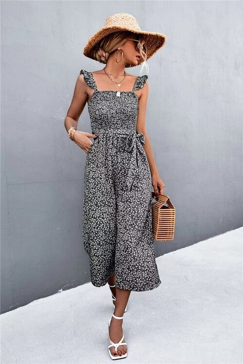 Woman wearing a floral dress and straw hat against a gray wall.