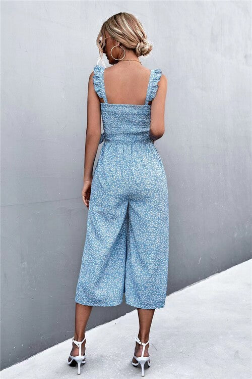 Woman wearing a blue floral jumpsuit against a gray wall.
