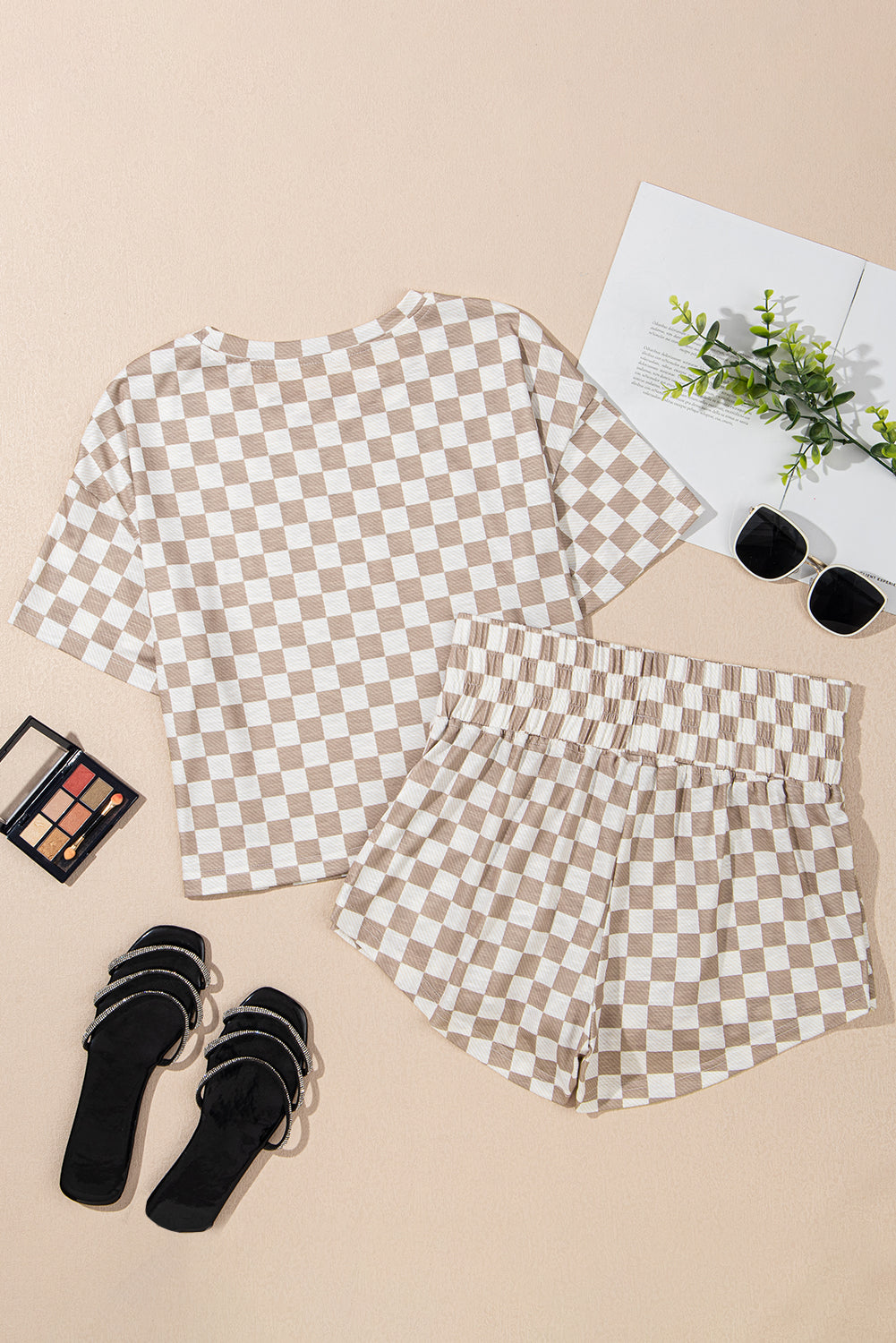 Checkered shirt and shorts set with black sandals, makeup palette, and plant on a beige surface