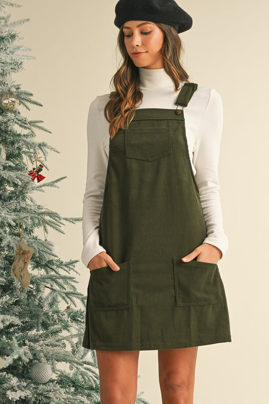 Woman wearing a green pinafore dress with a white long-sleeve shirt in front of a decorated Christmas tree.