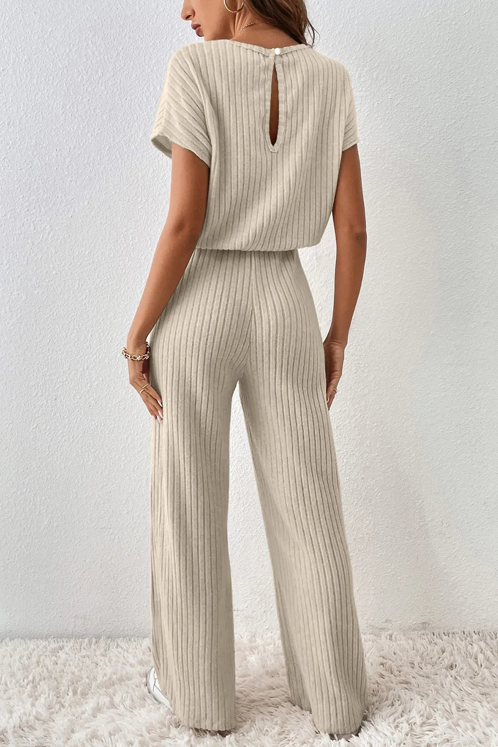 Woman wearing a beige ribbed jumpsuit against a white background