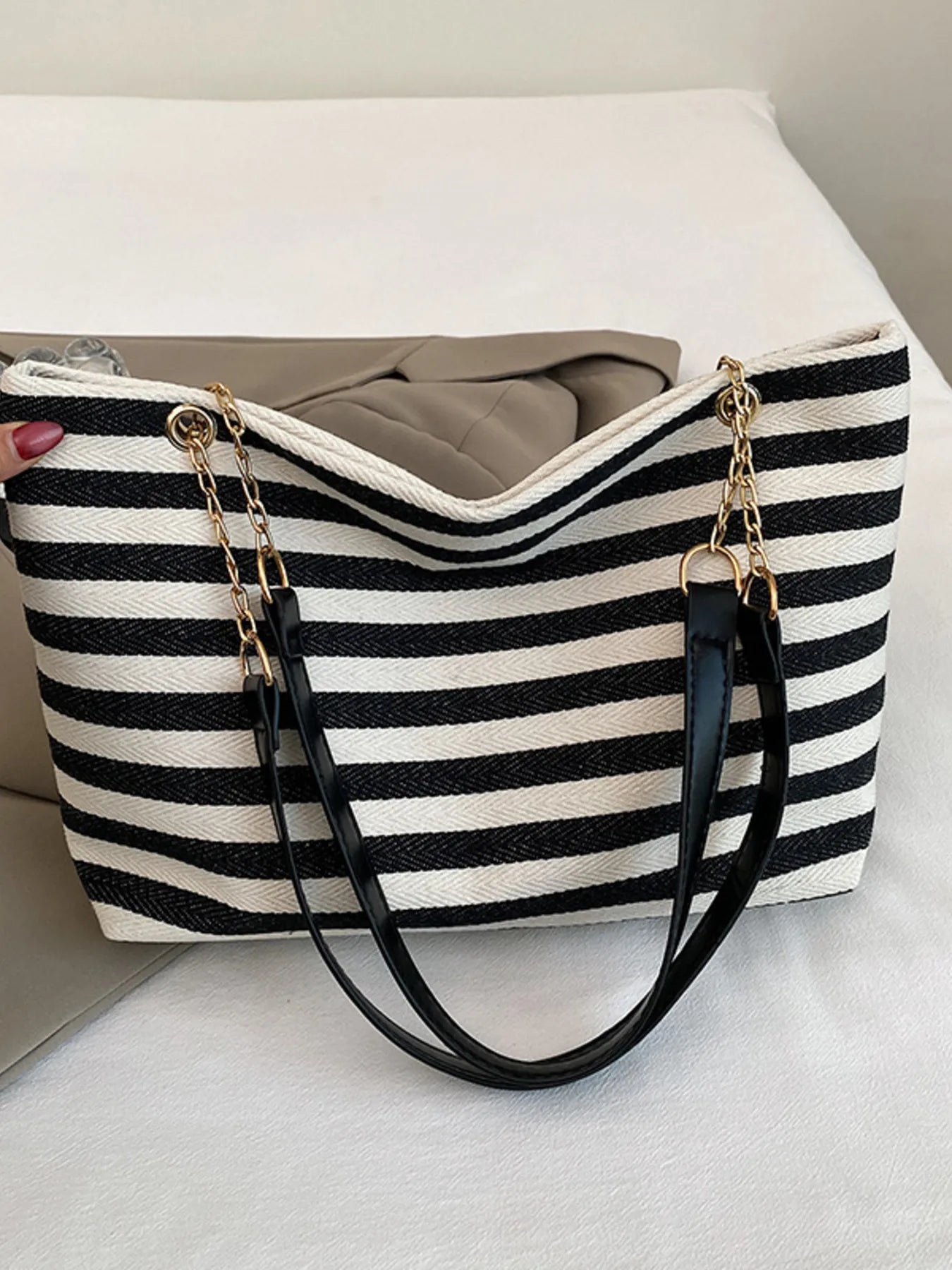 Black and white striped handbag with gold chain on a light background