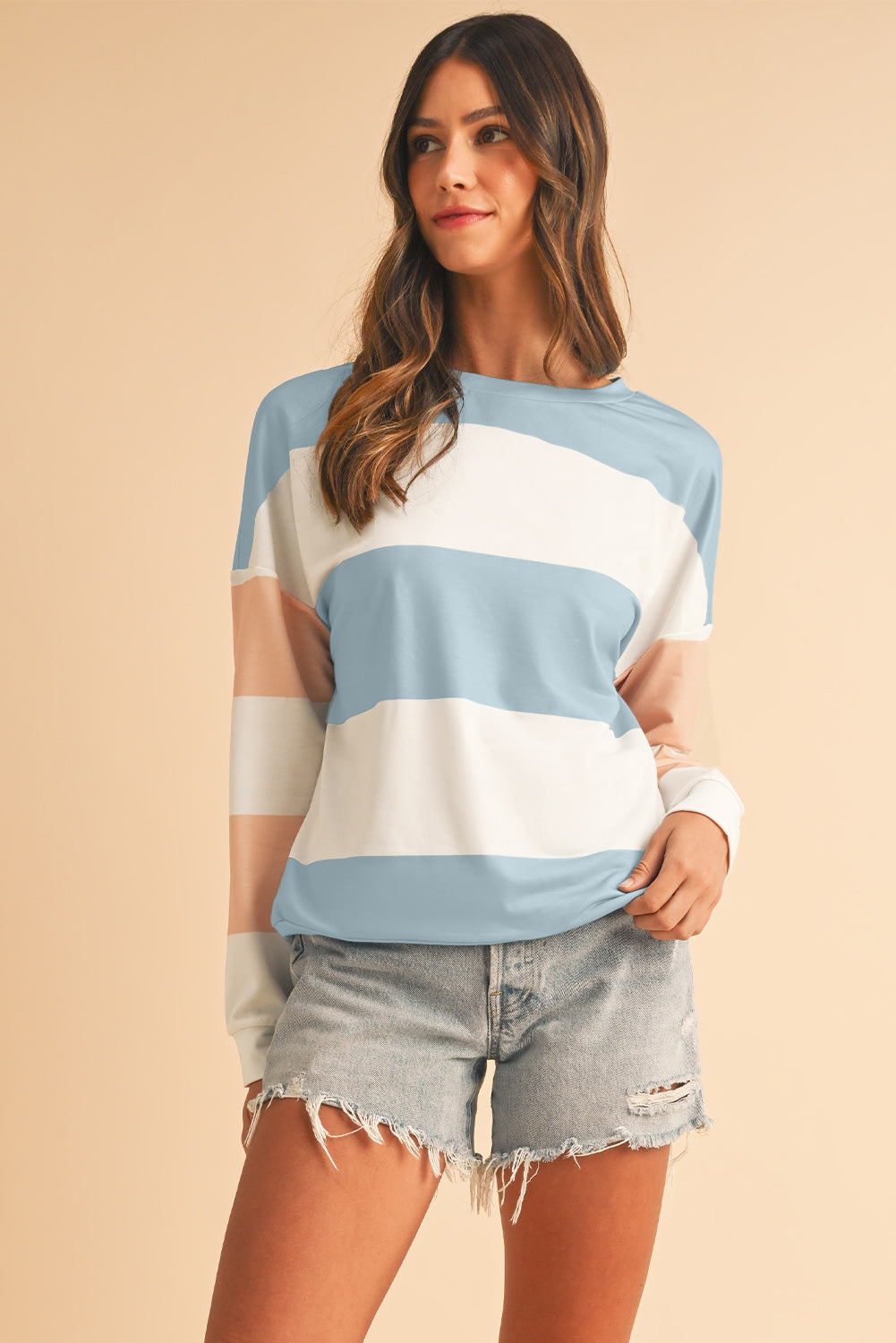 Woman wearing a striped shirt and denim shorts on a beige background
