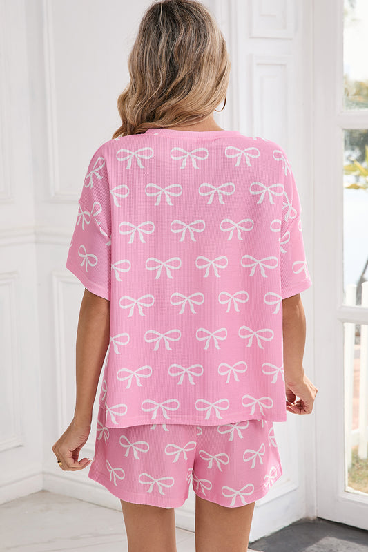 Woman wearing a pink pajama set with white bow patterns in a bright room.