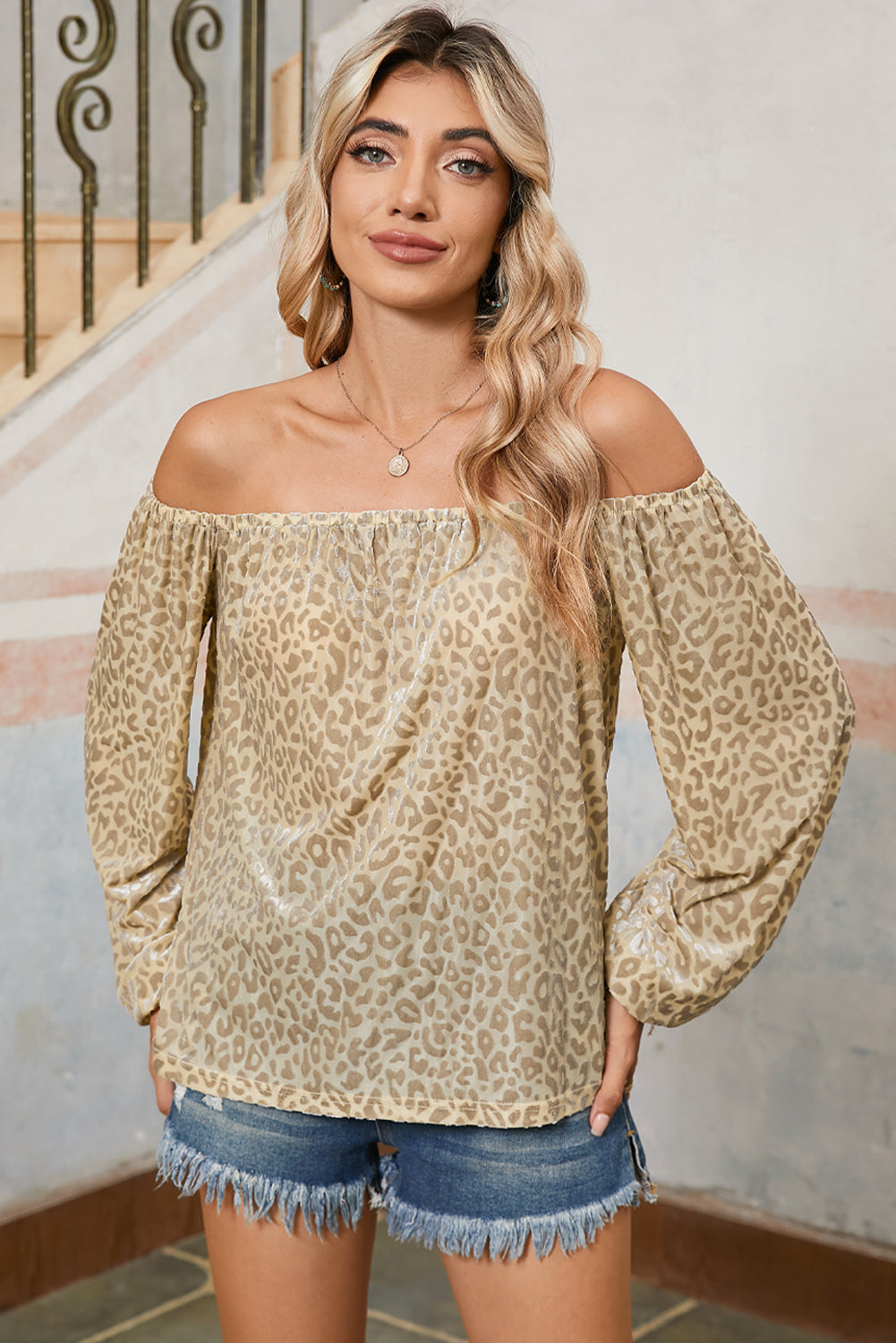 Woman wearing a leopard print off-shoulder top and denim shorts indoors.