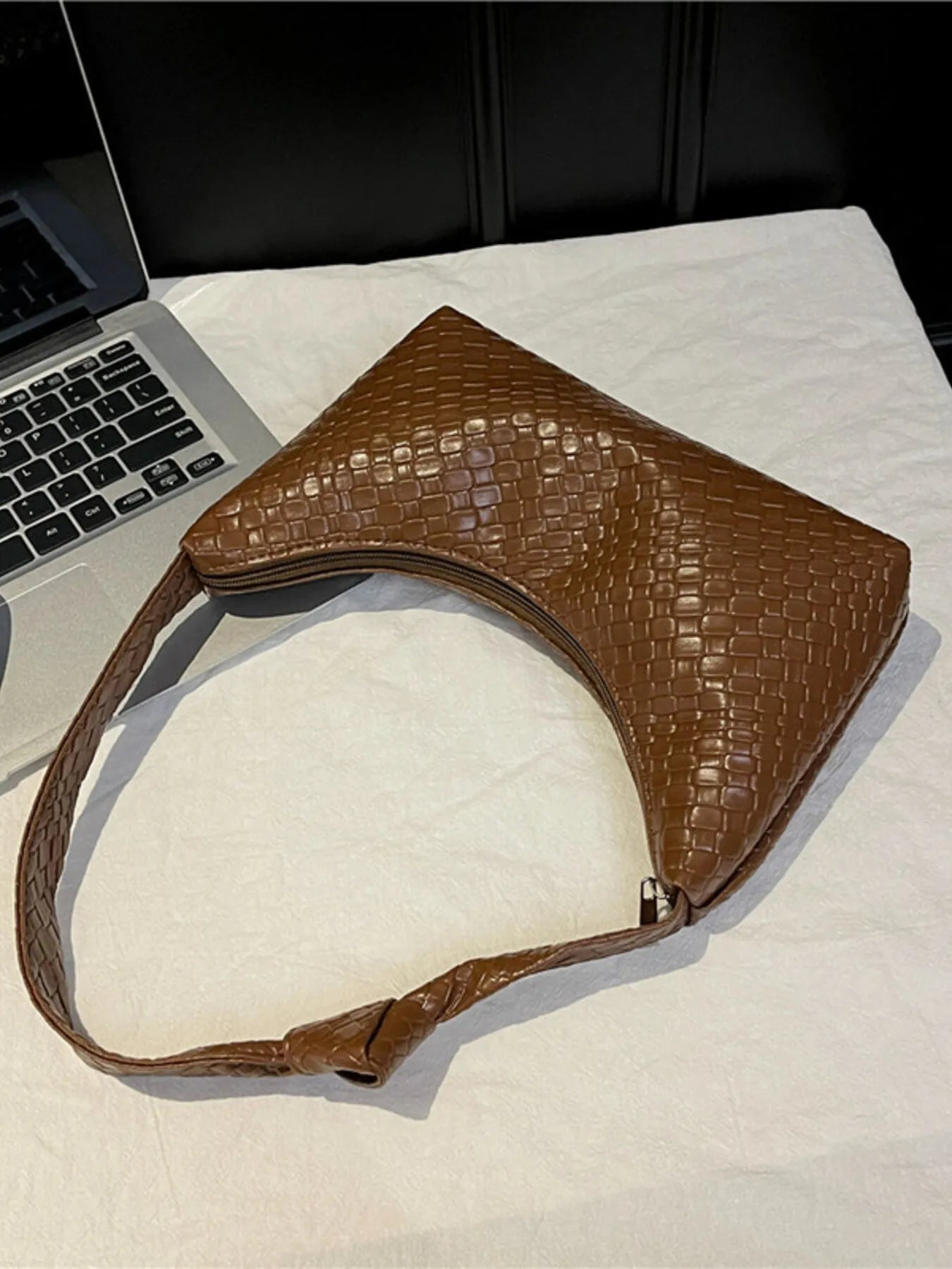 Brown textured handbag on a light surface with a laptop in the background
