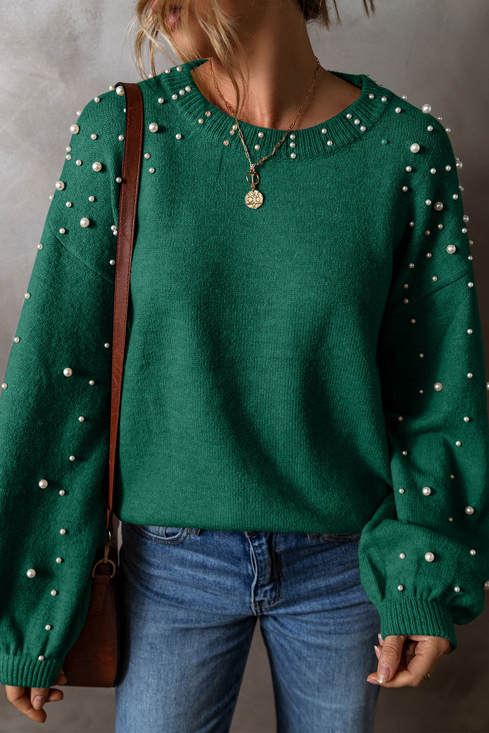 Green sweater with pearl embellishments worn by a person, with a neutral background