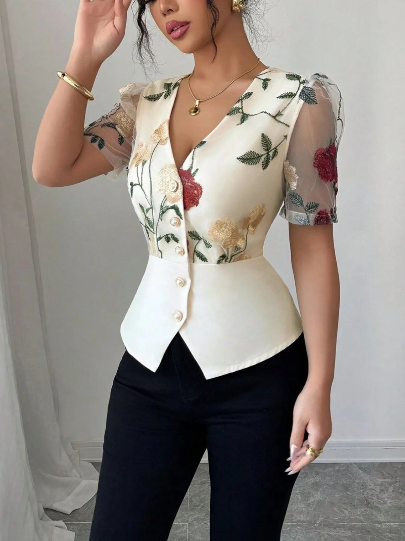 Woman wearing a floral blouse with sheer sleeves against a plain background