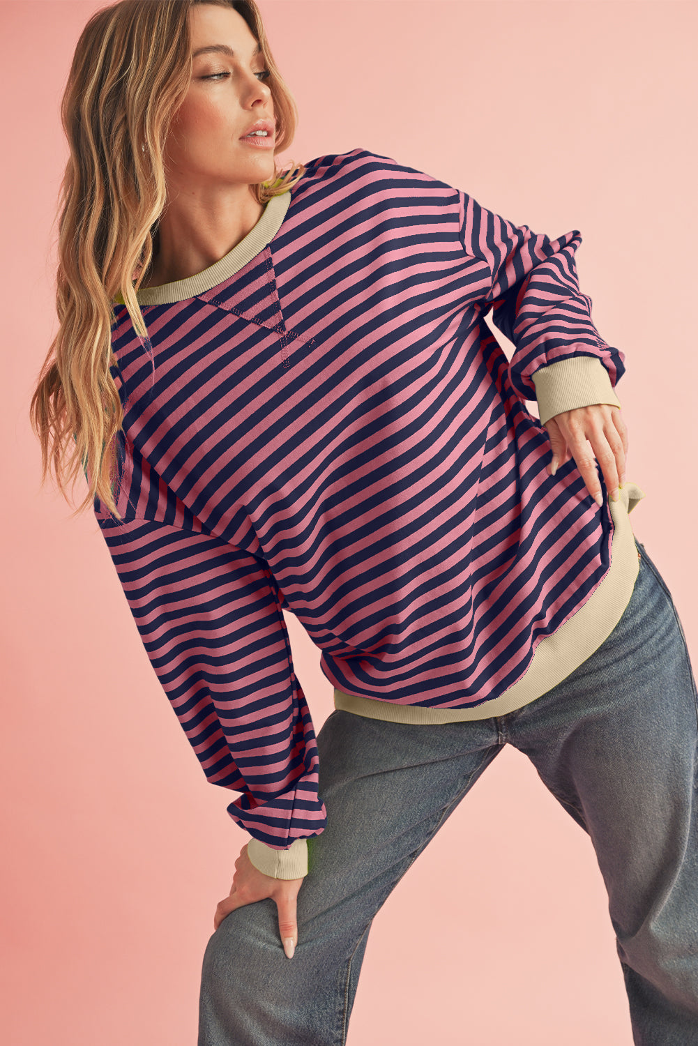 Woman wearing a striped sweater and jeans on a pink background