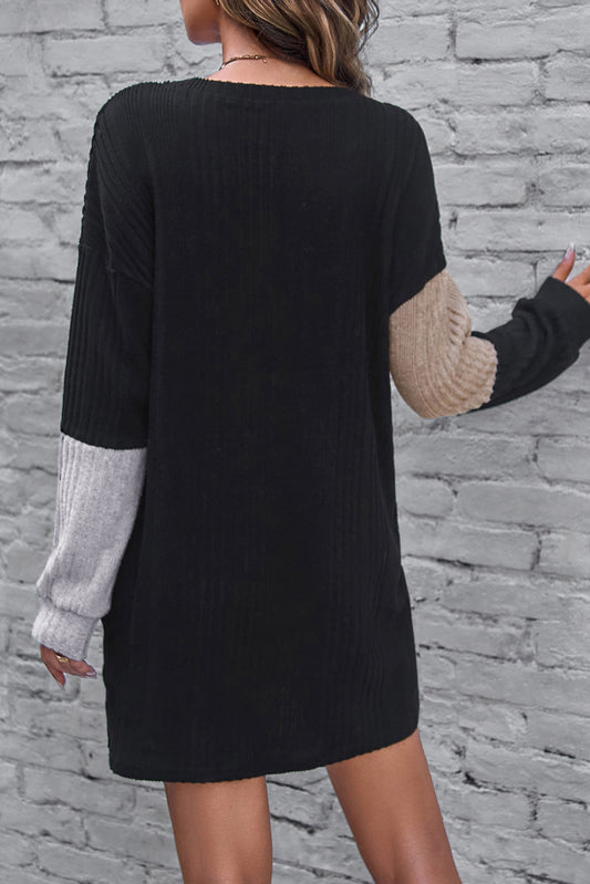 Black dress with color-blocked sleeves against a stone wall background