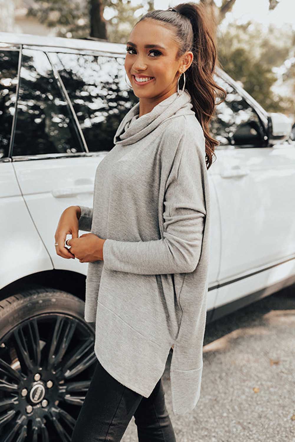 Woman in a gray sweater standing next to a white car
