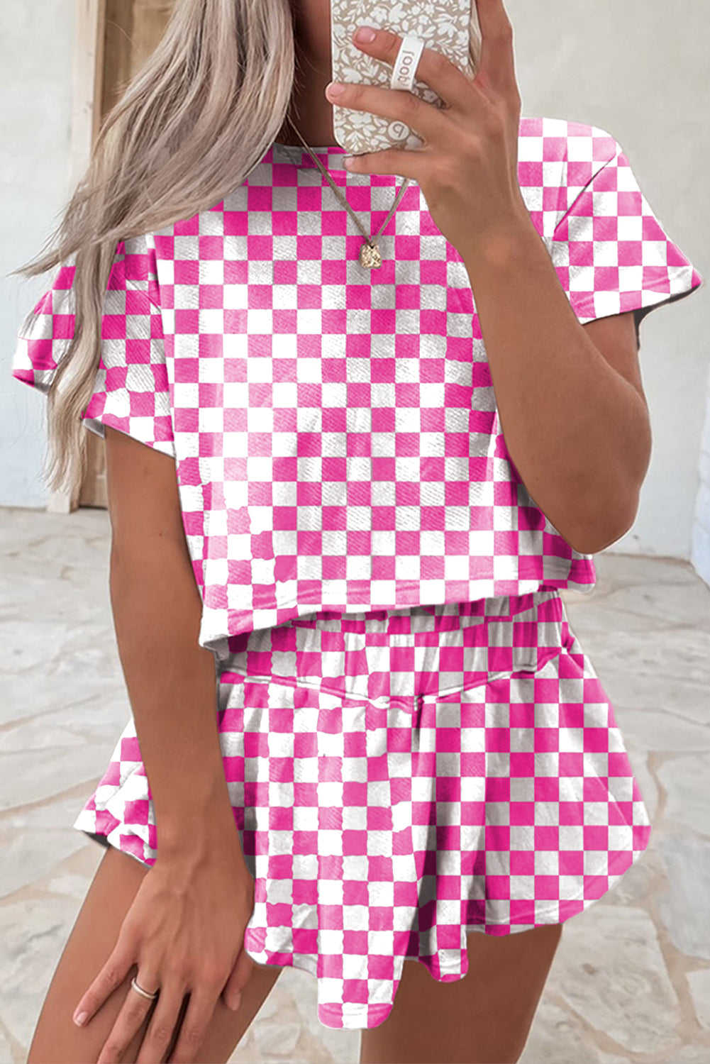 Person wearing a pink and white checkered outfit taking a mirror selfie.