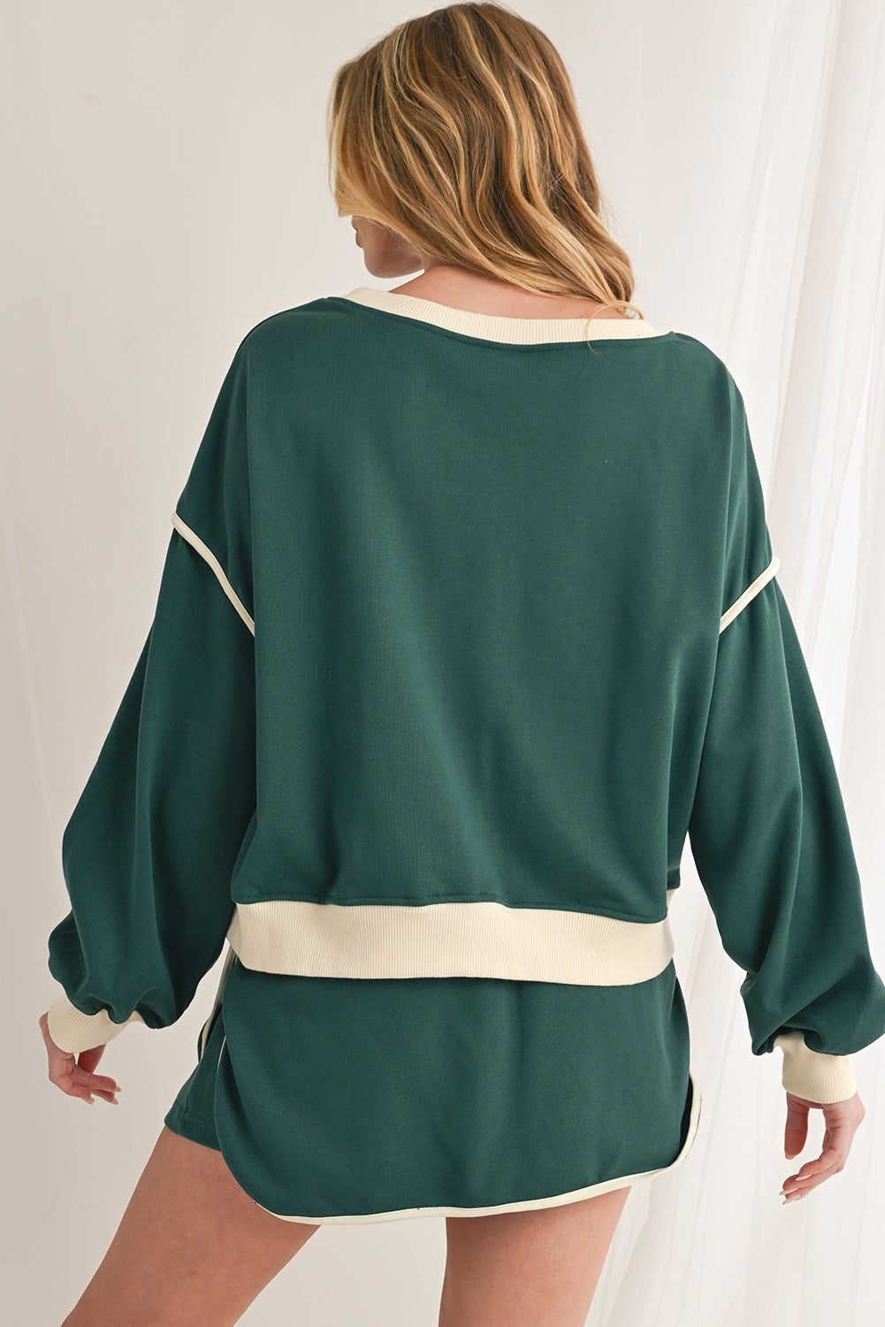 Green oversized sweater with white trim worn by a person on a plain background