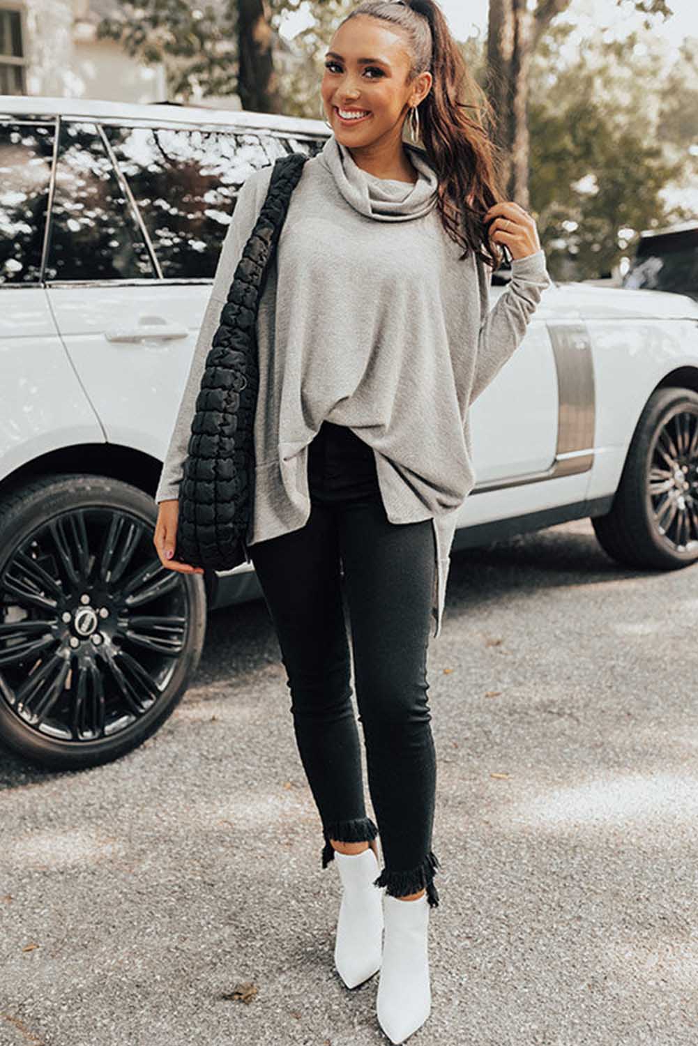 Woman in a gray sweater and black pants standing next to a white SUV.