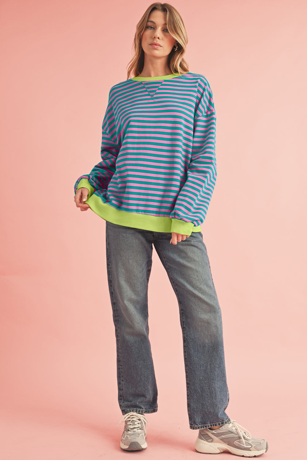 Woman wearing a striped sweater and jeans on a pink background