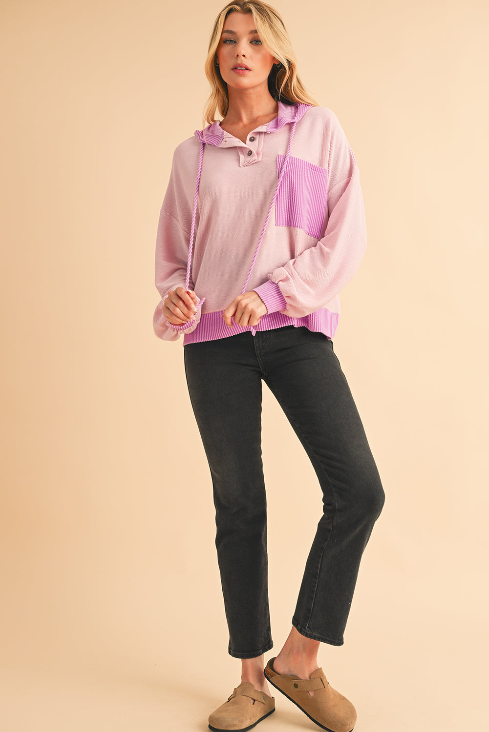 Woman wearing a pink and purple color-blocked hoodie with black pants on a beige background