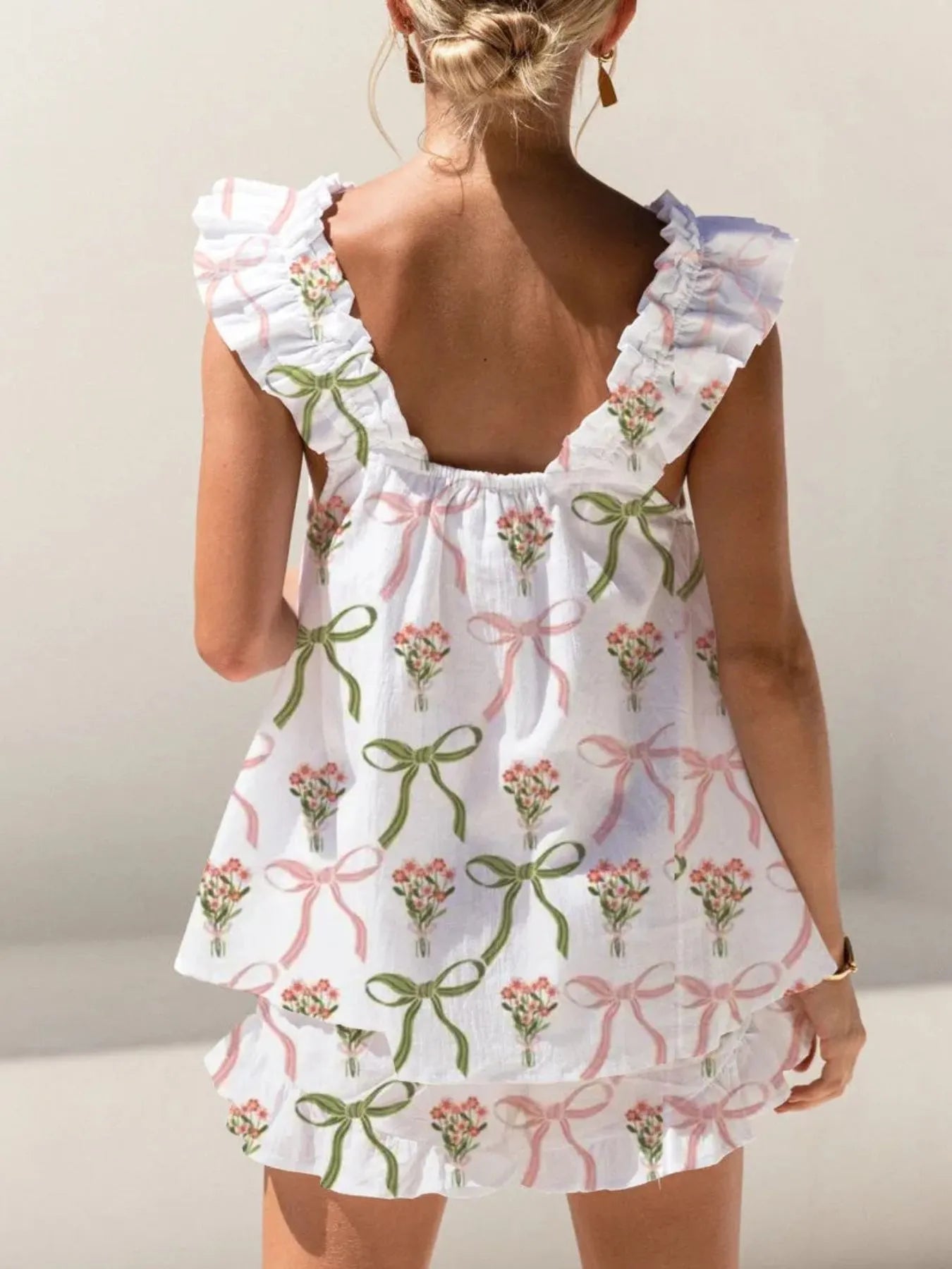 Woman wearing a white dress with floral and bow pattern on a plain background