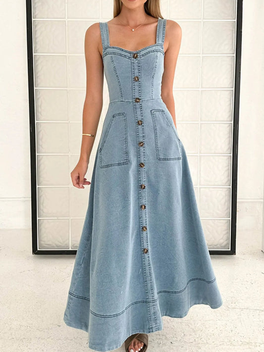 Woman wearing a denim dress with buttons against a white tiled wall.