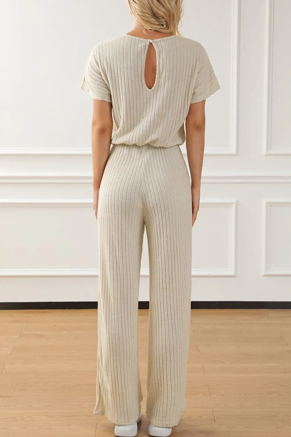 Person wearing a beige ribbed jumpsuit in a minimal indoor setting