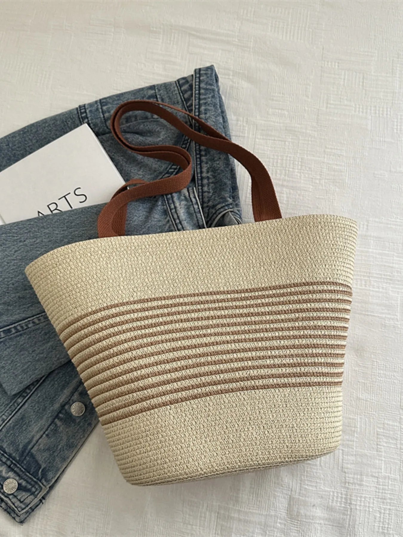 Beige woven tote bag with brown leather handle on a light gray surface