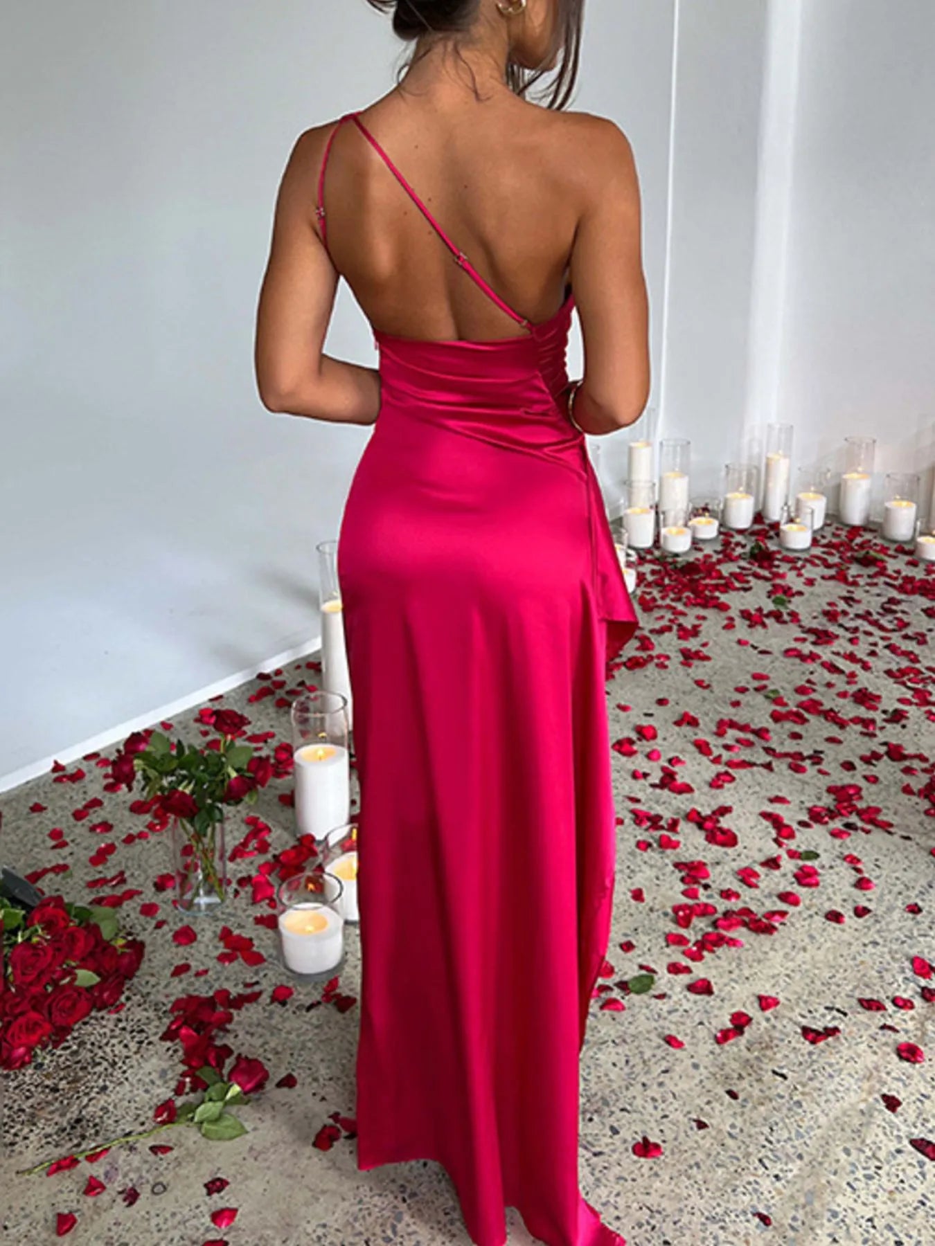 Woman in a red dress standing in a room with candles and rose petals on the floor.